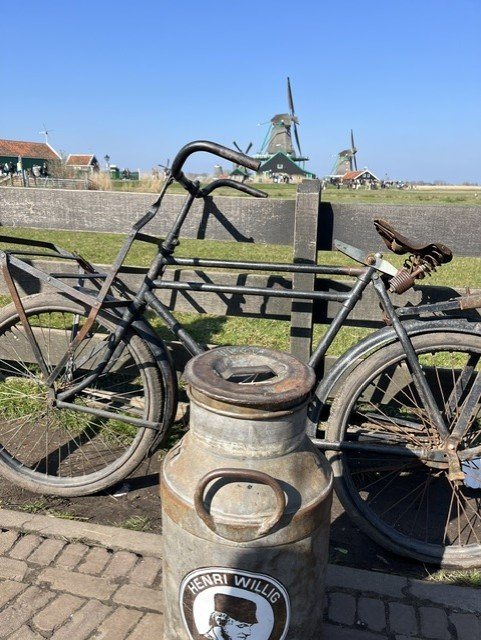 An old transport bicycle and a milk can with windmills in the background